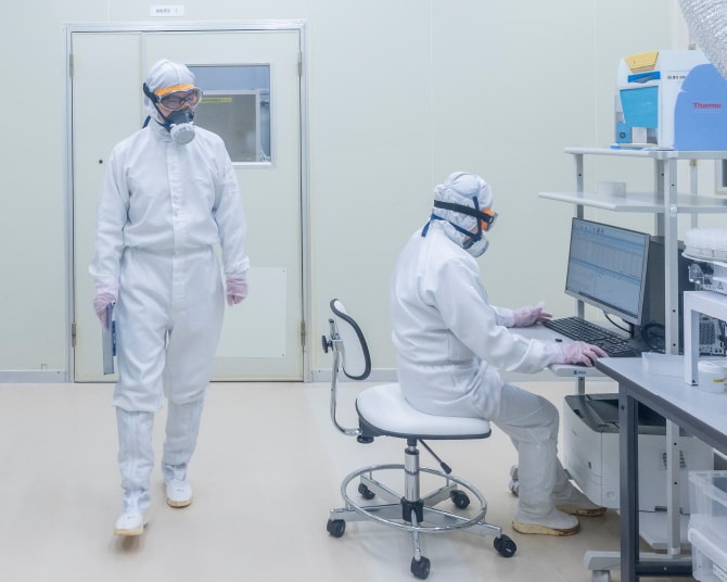 クリーンスーツにゴーグル、手袋、マスクをして働く2人の男性